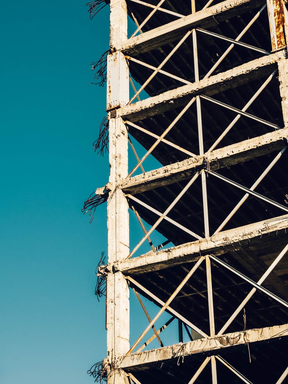 Rusty abandoned steel framework structure against a clear turquoise blue sky, showing deteriorating metal beams and triangular supports.