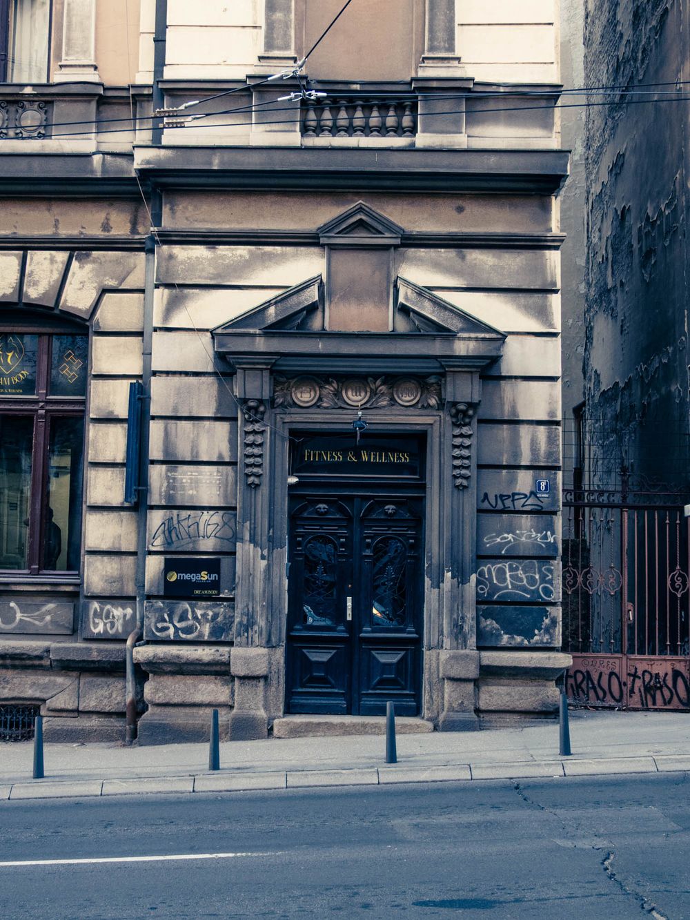 Historic stone building with ornate doorway, dark blue doors, graffiti-covered walls, and classical architectural details on a city street.