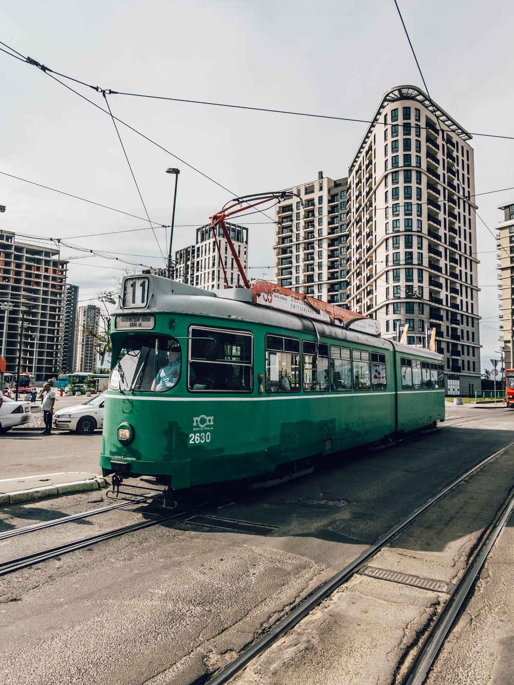 Green vintage tram number 11 on city tracks with modern high-rise buildings in the background.