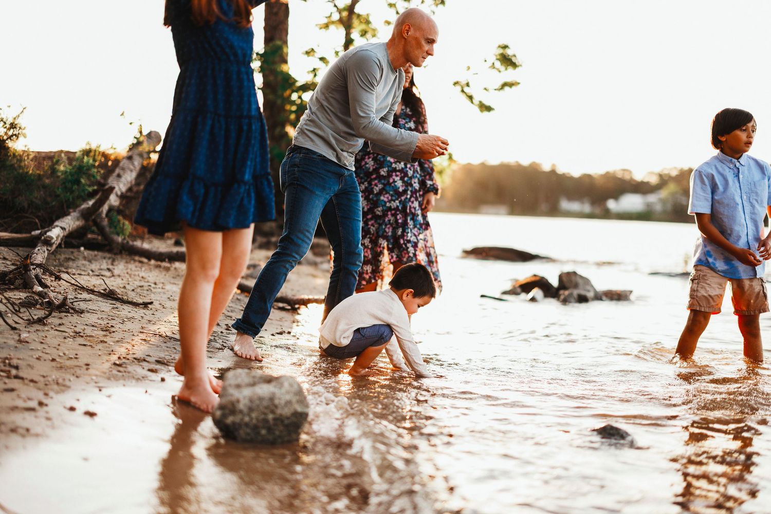 A group of people exploring a beach at sunset, splashing in the shallow water along the shoreline.