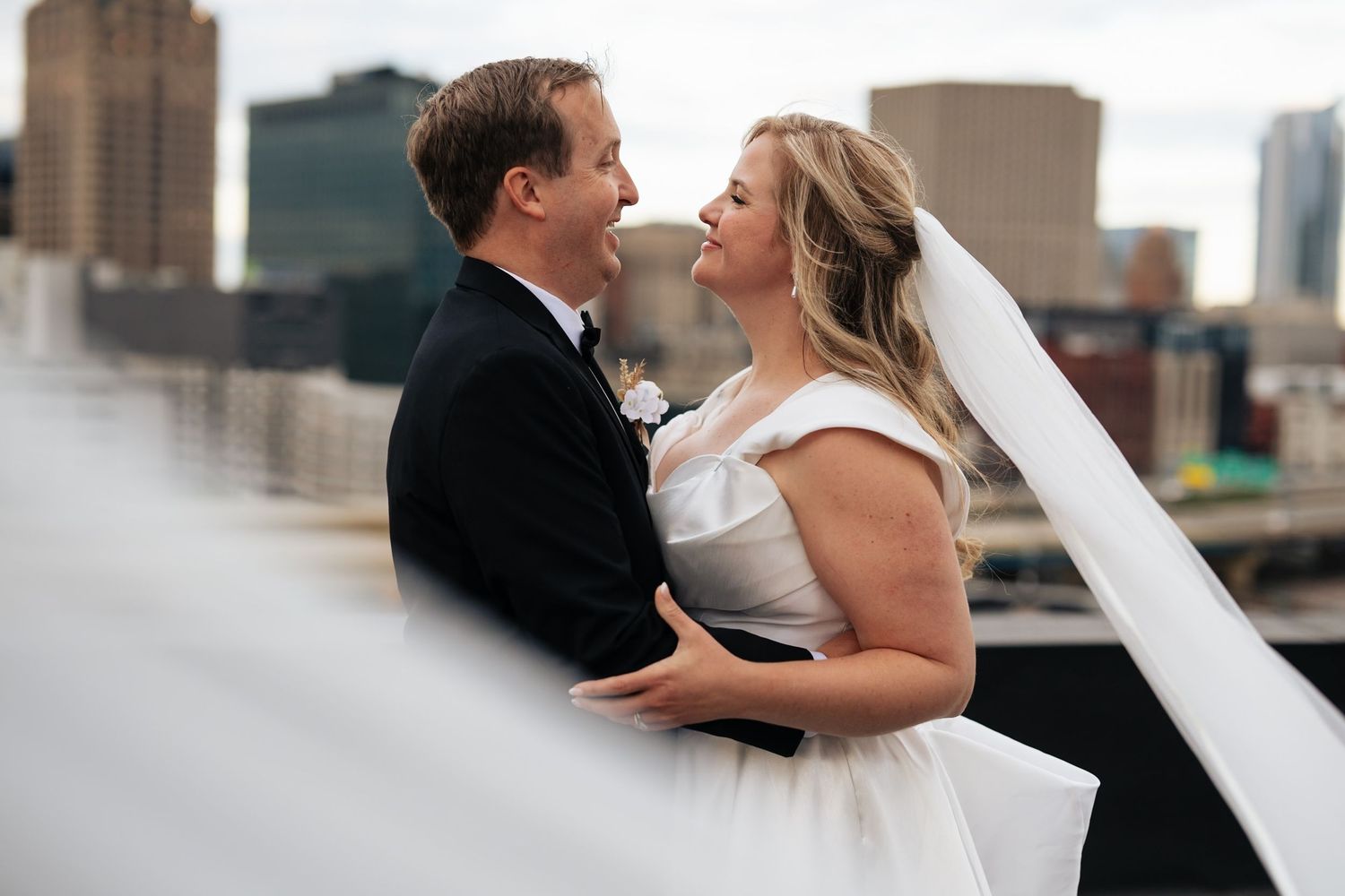 A romantic wedding couple shares intimate moments along a city waterfront with urban architecture in the background.