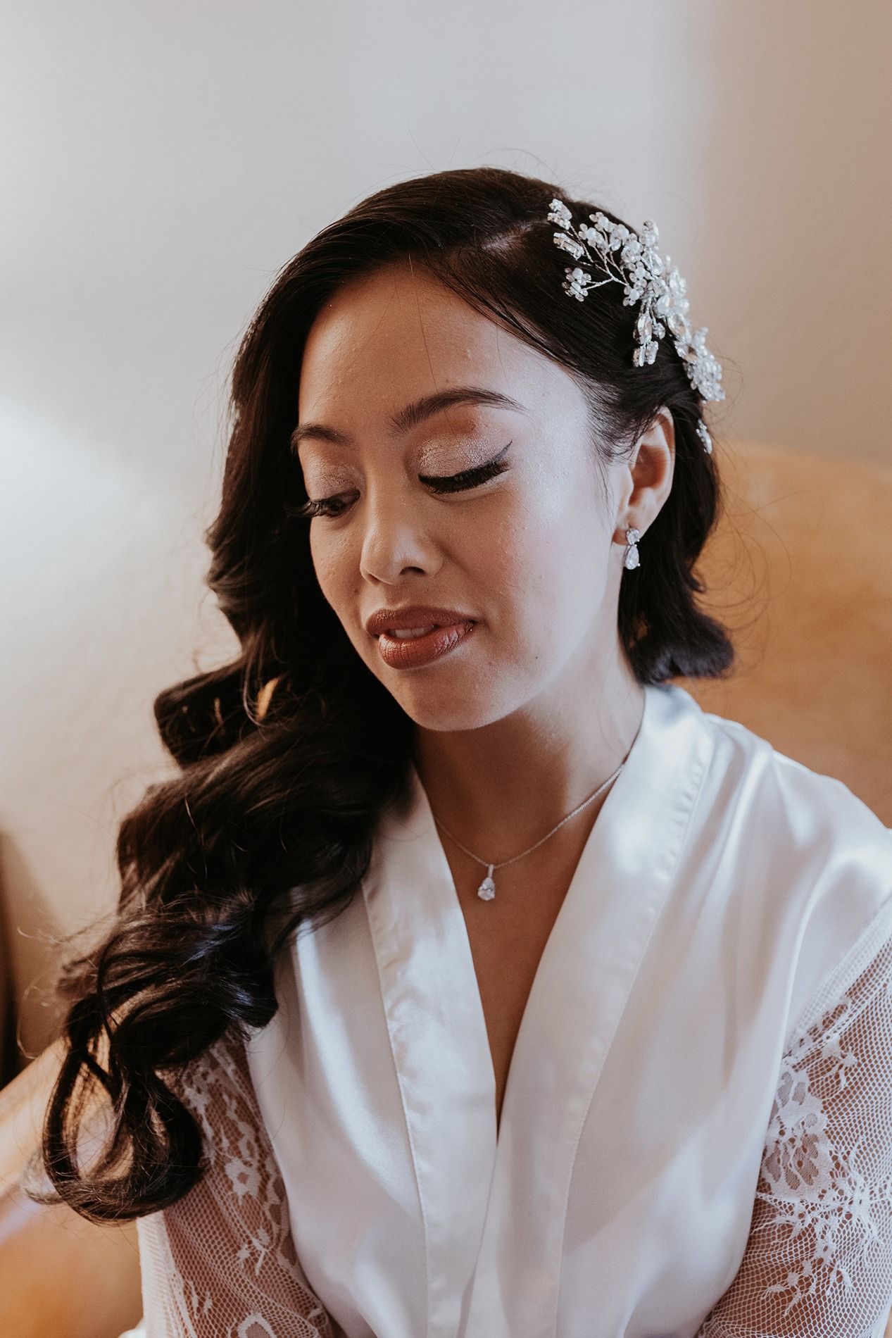 A bride in a white silk robe with delicate lace details gets ready for her wedding day at Rancho Bernardo Inn.