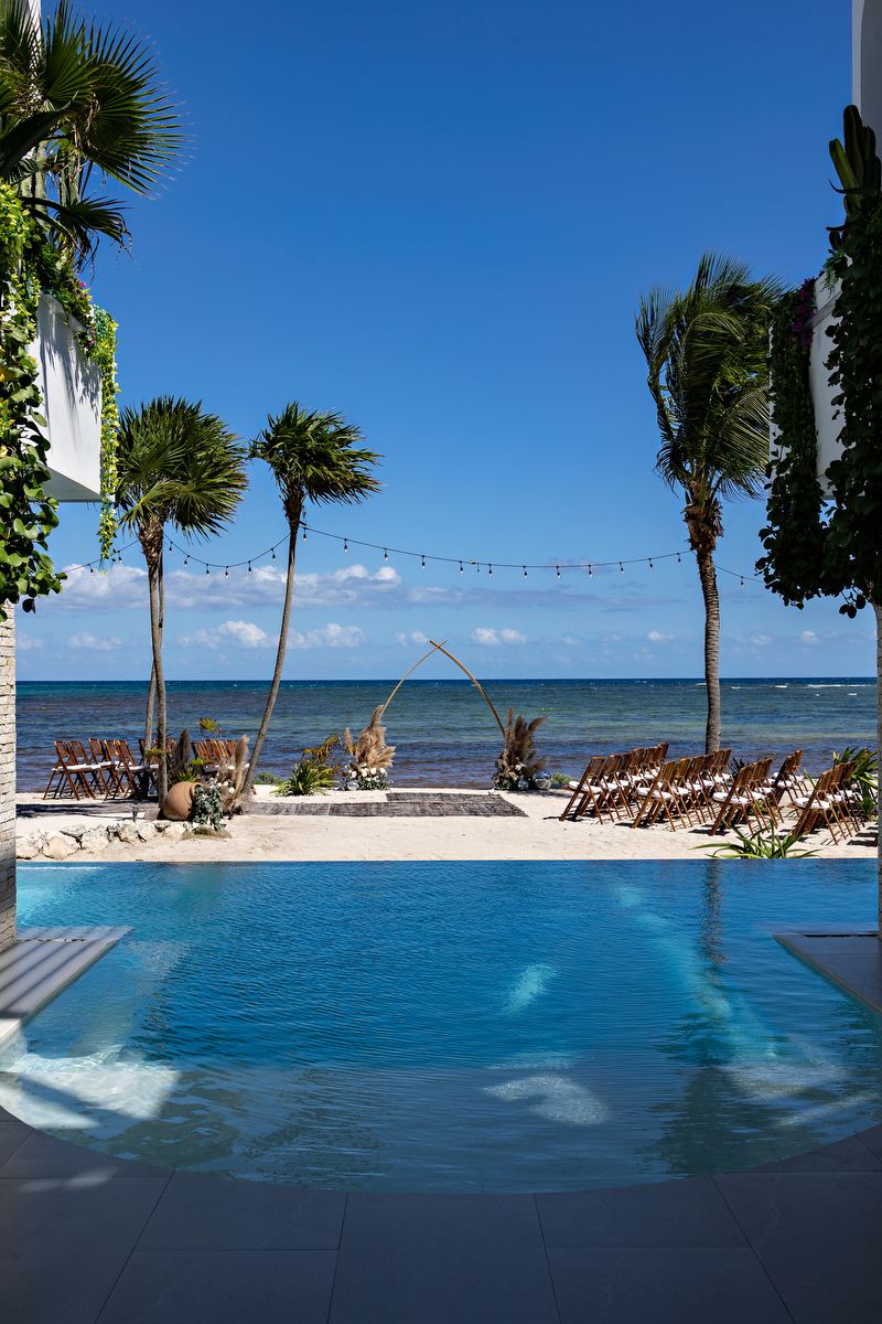 Luxury beachfront wedding setup in Tulum at Studio 54 villa, with ocean view ceremony aisle, wooden chairs, and tropical decor.