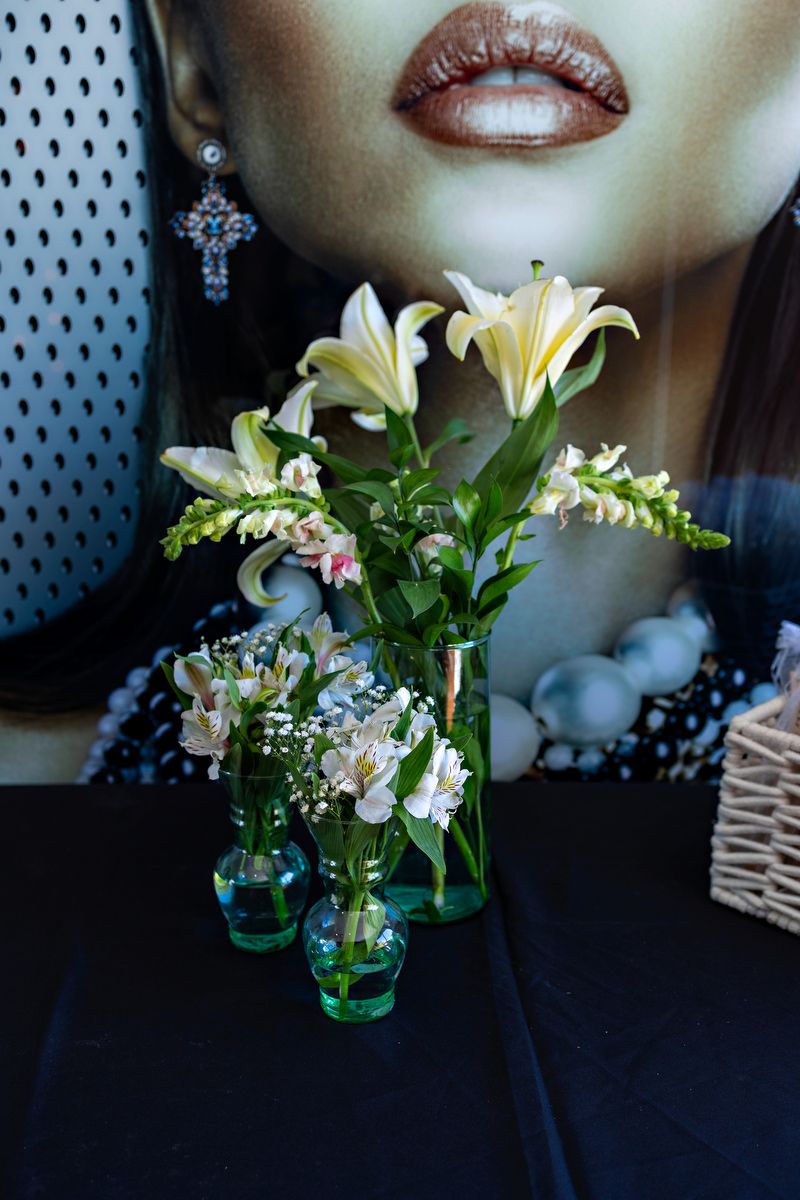 A white lily flower arrangement in a blue glass vase sits against a dark background with dramatic lighting.