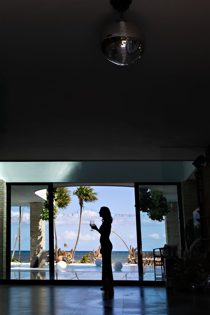 Silhouetted palm trees and ocean views through a panoramic window frame create a tropical resort atmosphere.