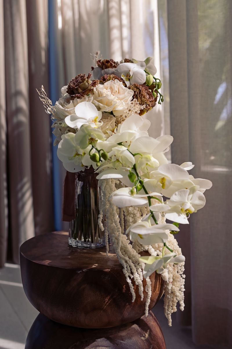 Elegant wedding floral arrangement with orchids and neutral tones in soft window light at Tulum luxury villa wedding.