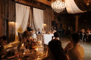 Rustic barn wedding reception illuminated by warm chandelier lighting and white fabric draping across the ceiling.