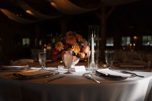 Elegant place settings with white plates and wine glasses on dark wooden tables in a dimly lit restaurant atmosphere.