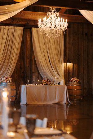 Elegant wedding reception venue with white drapes, crystal chandeliers, and rustic wooden walls illuminated by warm lighting.