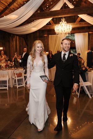Couple dances together in an elegant rustic wedding venue with draped fabric and chandeliers overhead.
