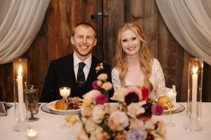 A wedding reception table setting with white linens, candles, and floral centerpieces at an elegant indoor venue.