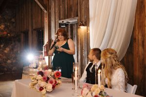 Wedding reception dinner table with candlelight and floral centerpieces in a rustic barn setting.