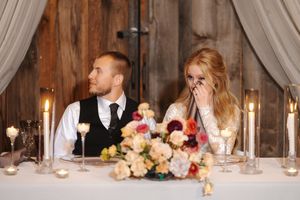 Wedding reception head table decorated with white linens, candles and floral arrangements in rustic barn setting.