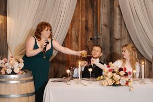 Wedding party reacts emotionally during heartfelt reception toasts at rustic venue with elegant white draping.