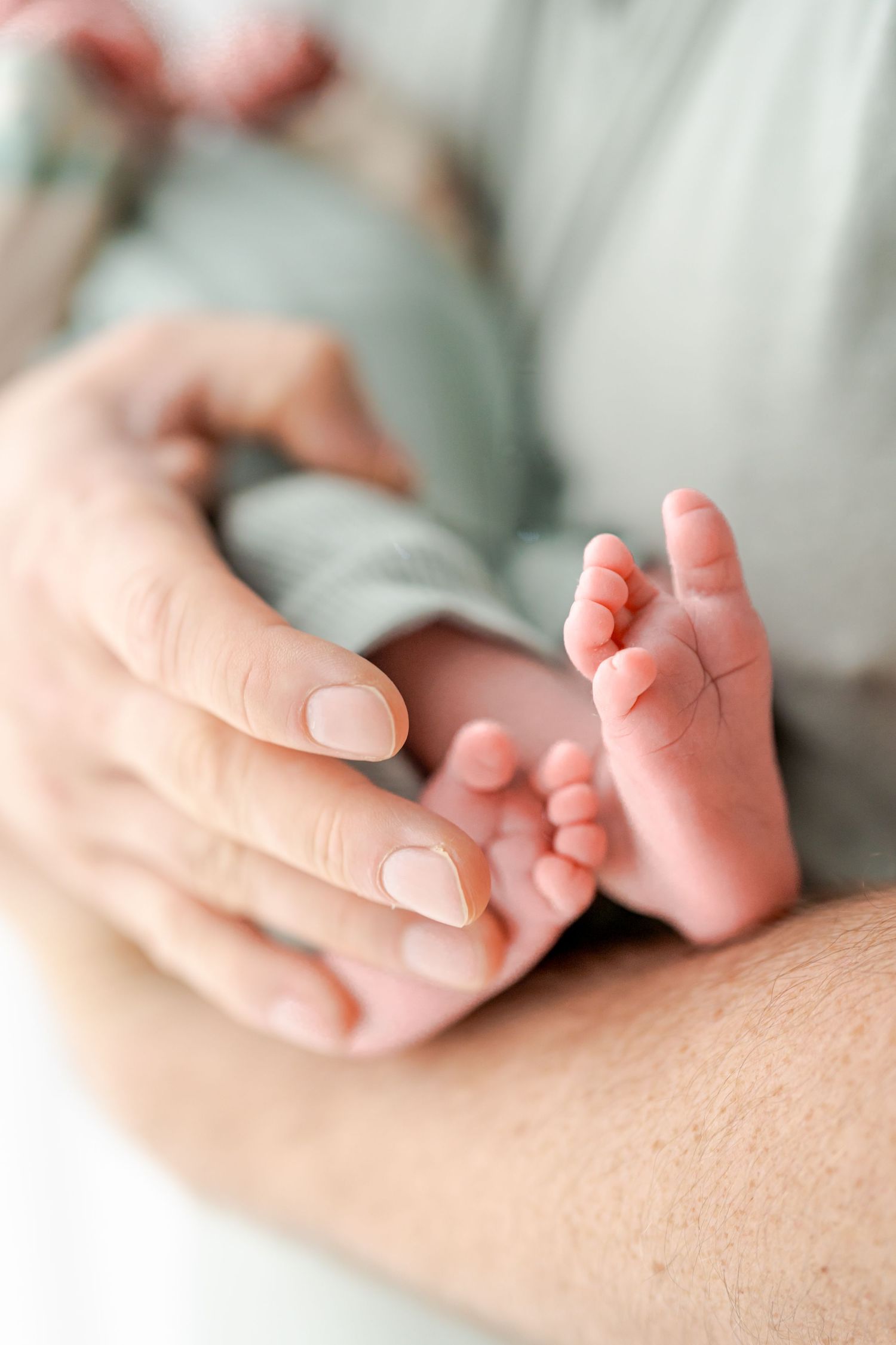 Family lying together on white bedding while sharing tender moments with newborn baby in soft natural light.