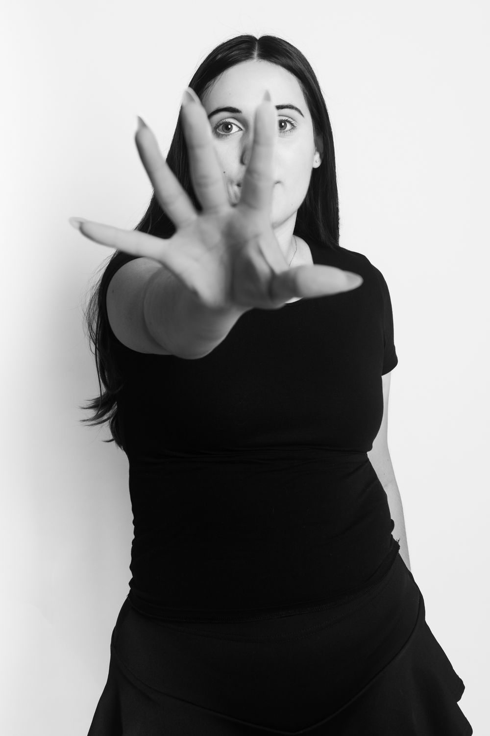 Black and white photo of woman in black dress reaching hand toward camera dramatically.