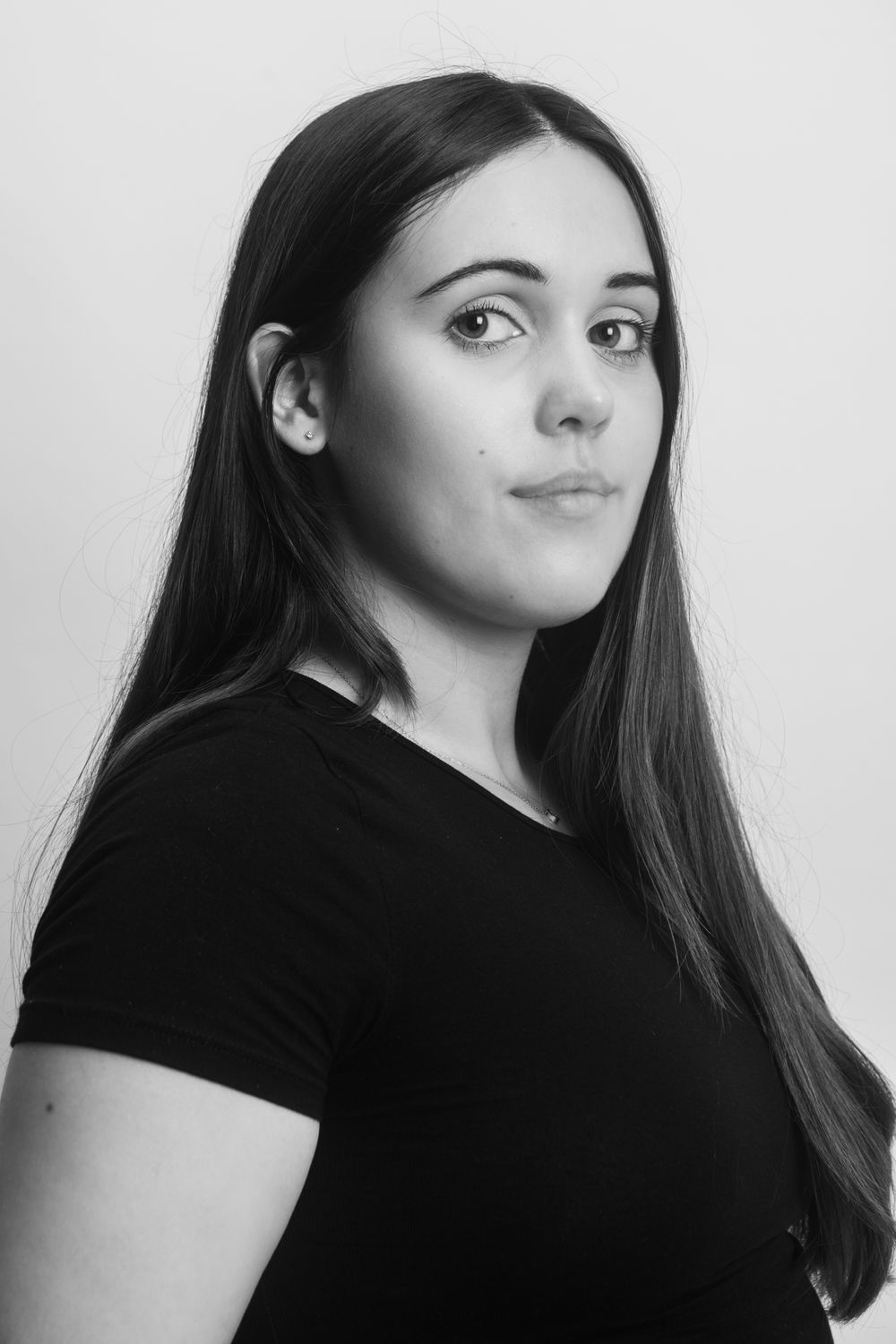 Black and white portrait of young woman with long dark hair wearing black t-shirt.