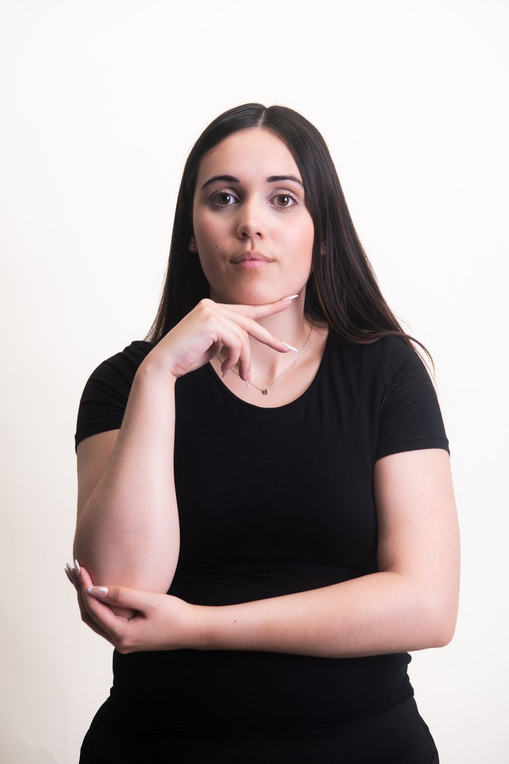 Portrait of a young woman in black t-shirt resting chin on hand in thoughtful pose against white background.