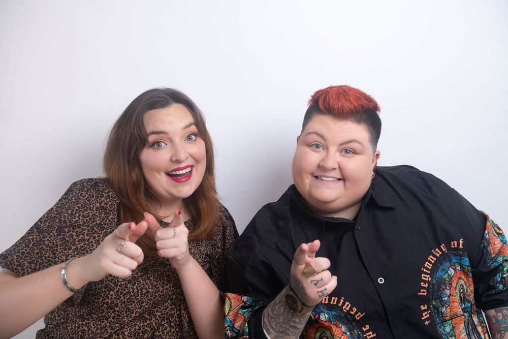 Two cheerful women pointing at the camera and smiling in a fun portrait against a white background.