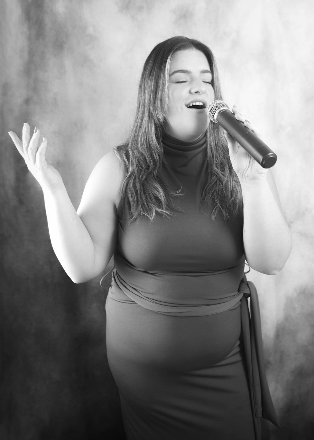 Black and white photo of a woman singing emotionally into a microphone on a smoky stage in a sleek dress.