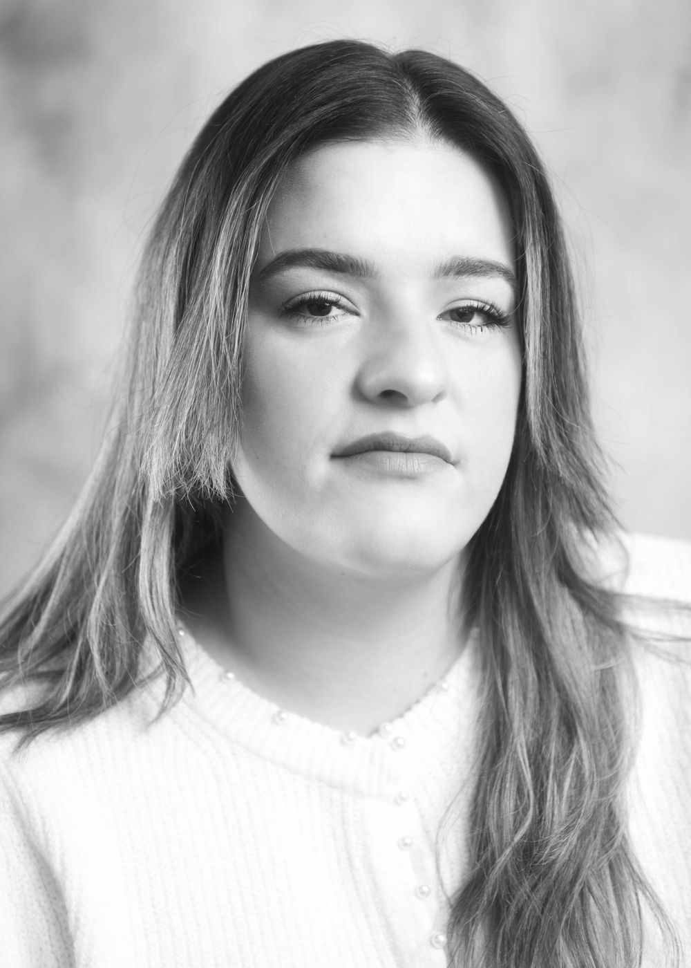 Black and white headshot of young woman with long highlighted hair in white top.