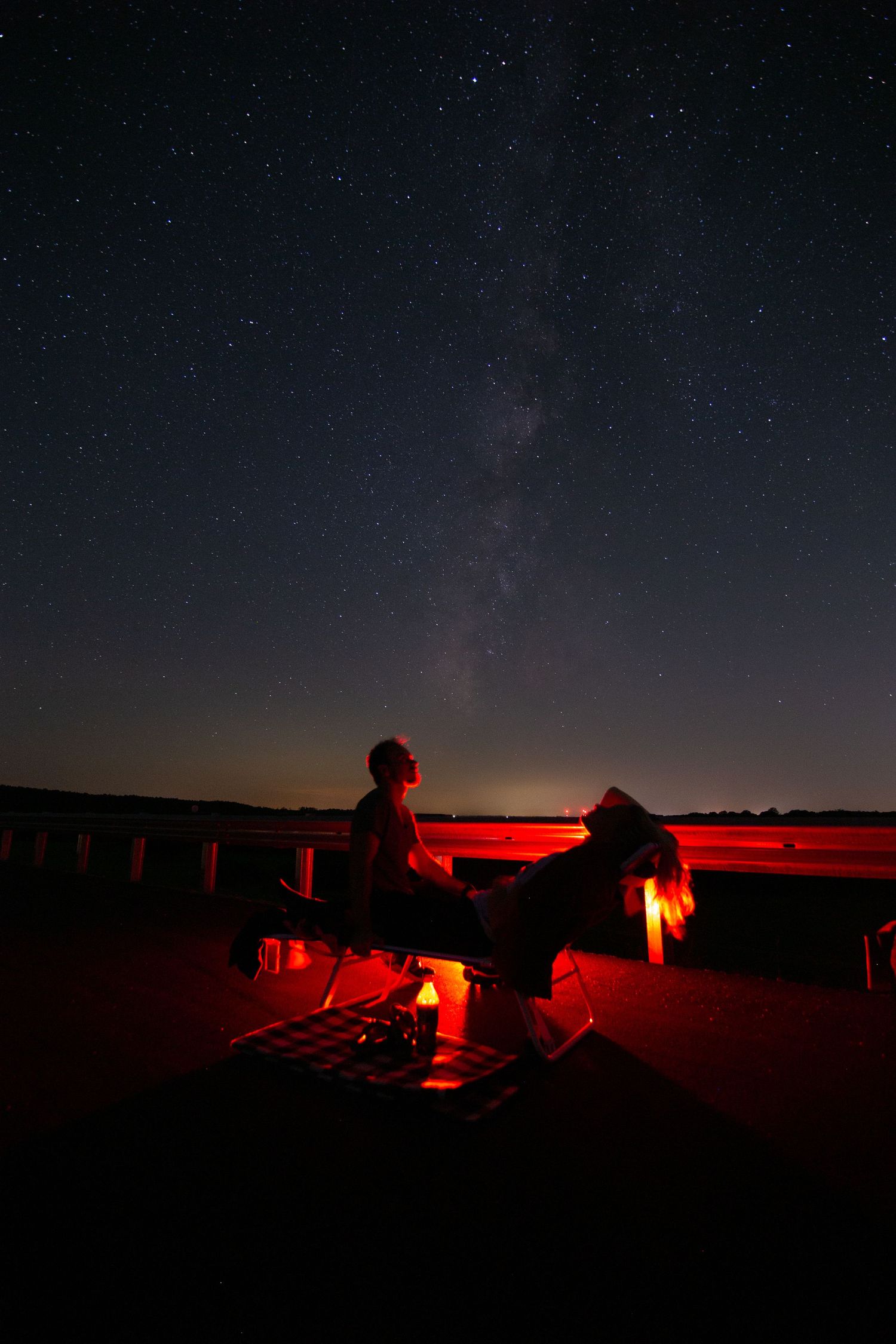 A panoramic view of stargazers using red lights to observe the night sky while preserving their night vision.