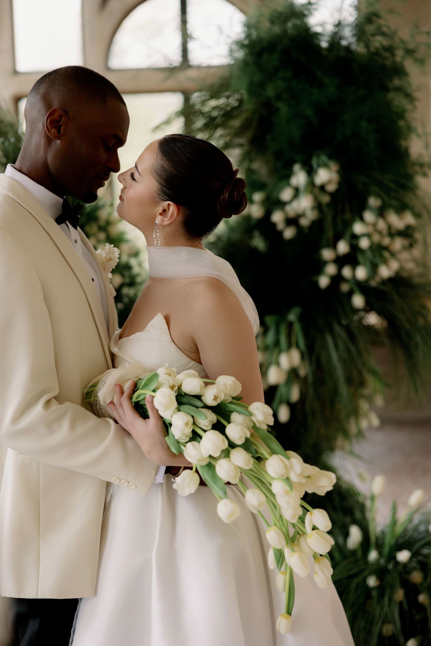 A romantic wedding couple in white attire share tender moments with a cascading bouquet of white tulips.