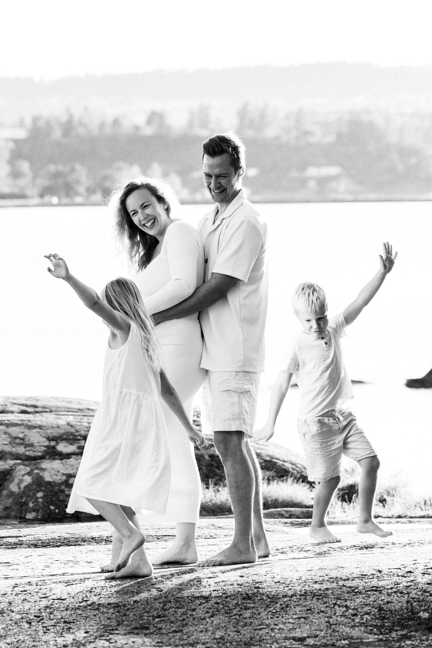 A series of black and white beach photos showing a family in white clothing playing and posing together on the shore.