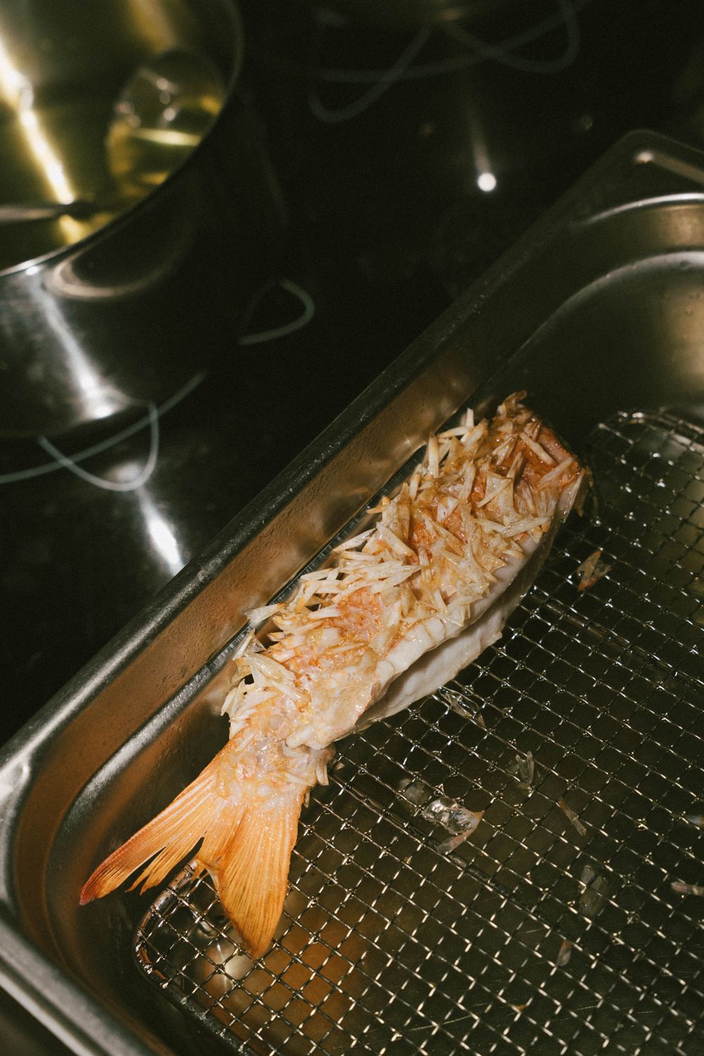 Grilled whole fish with crispy golden scales resting on a metal grill rack inside a Japanese fish broiler.