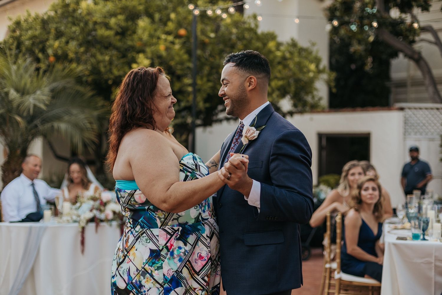 A groom in a navy suit shares a mother-son dance at an outdoor wedding reception with string lights at Darlington House.