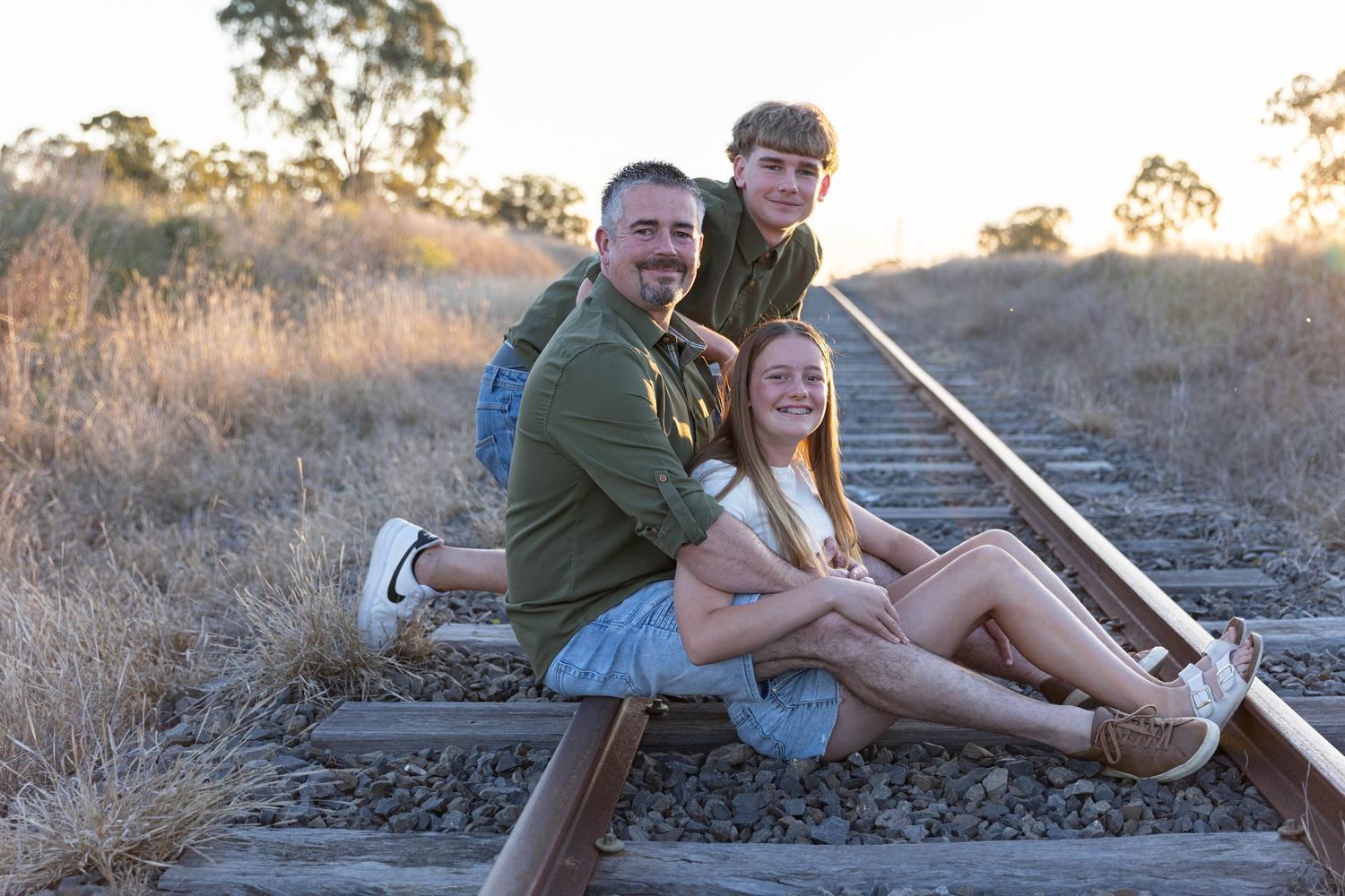 Father and children sitting on railway line at sunset during a father's day mini photo shoot