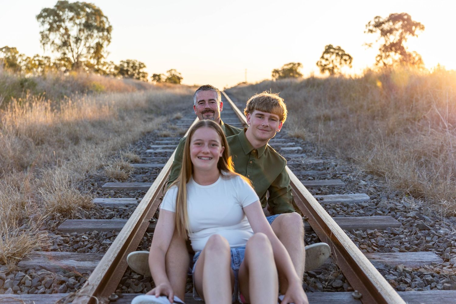 Father and children sitting on railway line at sunset during a father's day mini photo shoot