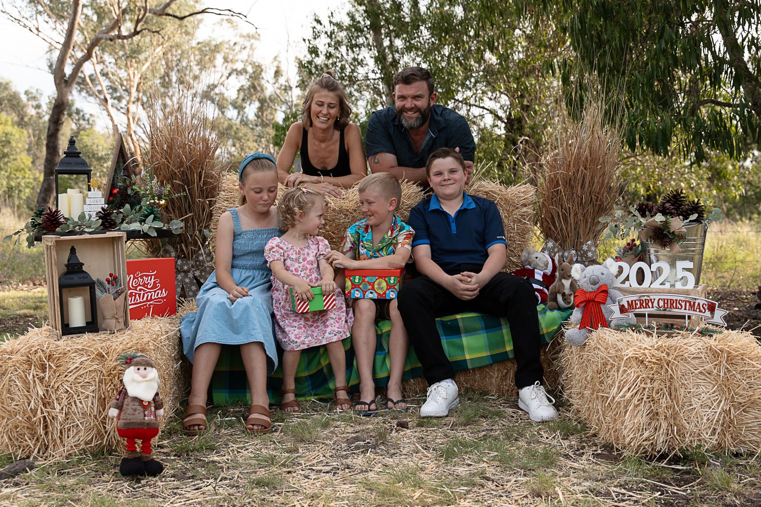 family sitting on hay bales at country, rustic christmas mini photo shoot