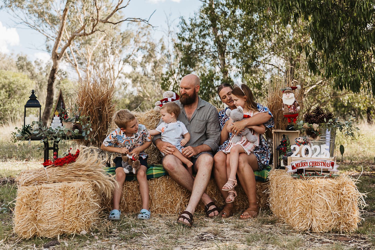 family sitting on hay bales at country, rustic christmas mini photo shoot