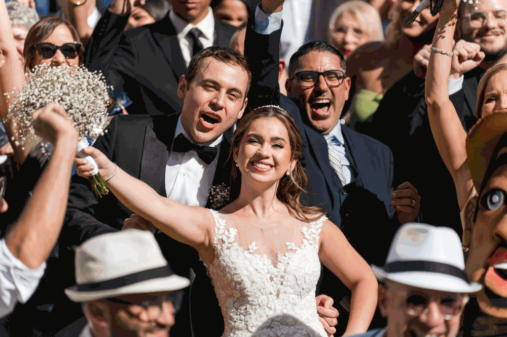 Bride and groom celebrating with guests and traditional vejigante masks during plena parade in Old San Juan