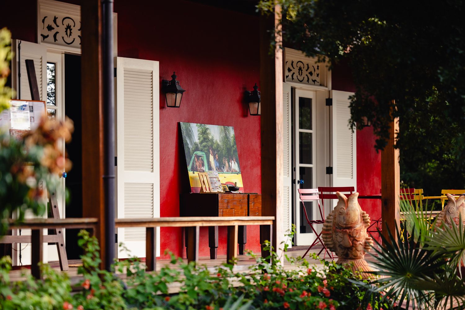 Charming red colonial building with white shutters, a painted canvas, and lush garden surroundings.
