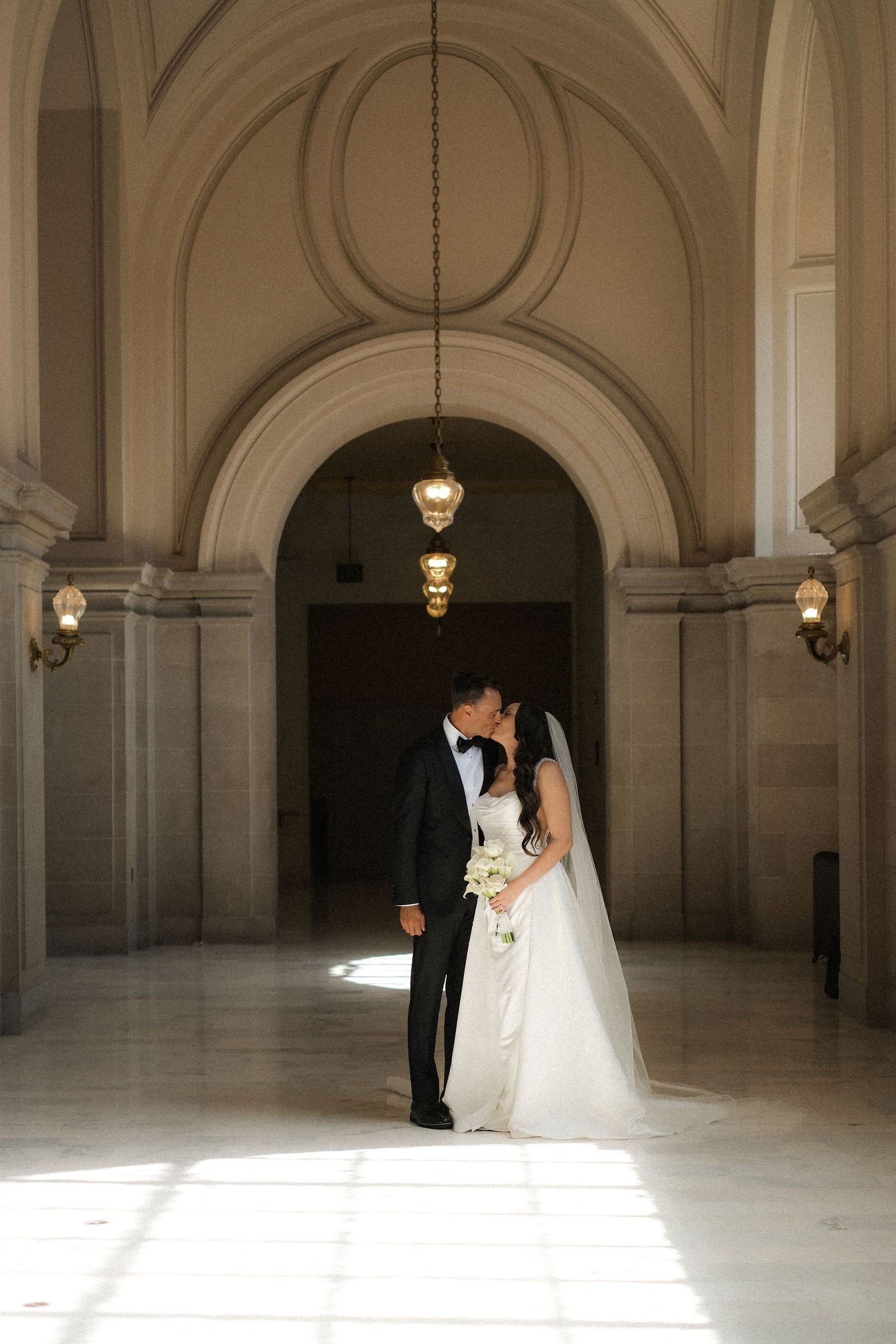 Wedding couple in an elegant arched hallway with dramatic lighting.