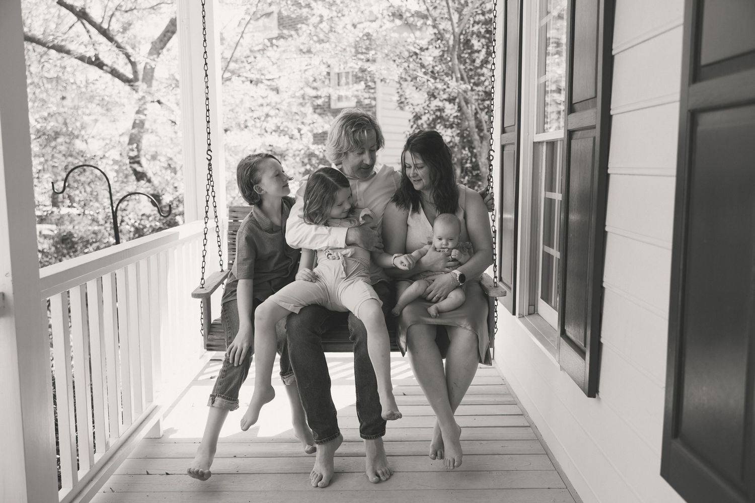 Black and white photo of a joyful family laughing together on a charming porch swing.