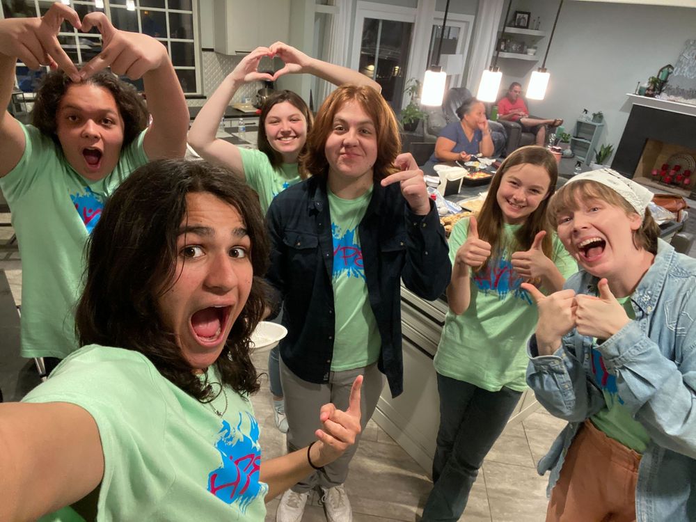 Group of teens in matching green t-shirts taking a fun selfie together indoors.