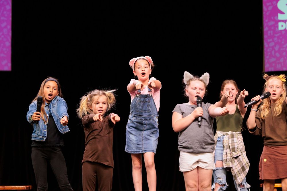 Young girls performing on stage with microphones during a children's theater or talent show.