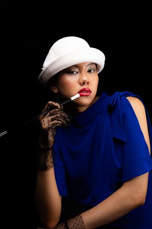 Image of a girl in a white, wool, bowler hat with polka dot, clear black gloves, with a cigarette holder, looking at the camera