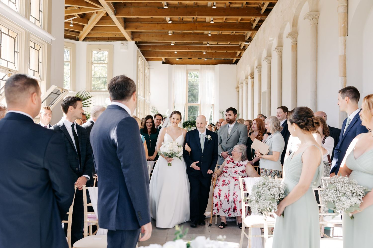Wedding guests mingle and celebrate in a rustic venue with exposed wooden beams and natural lighting.