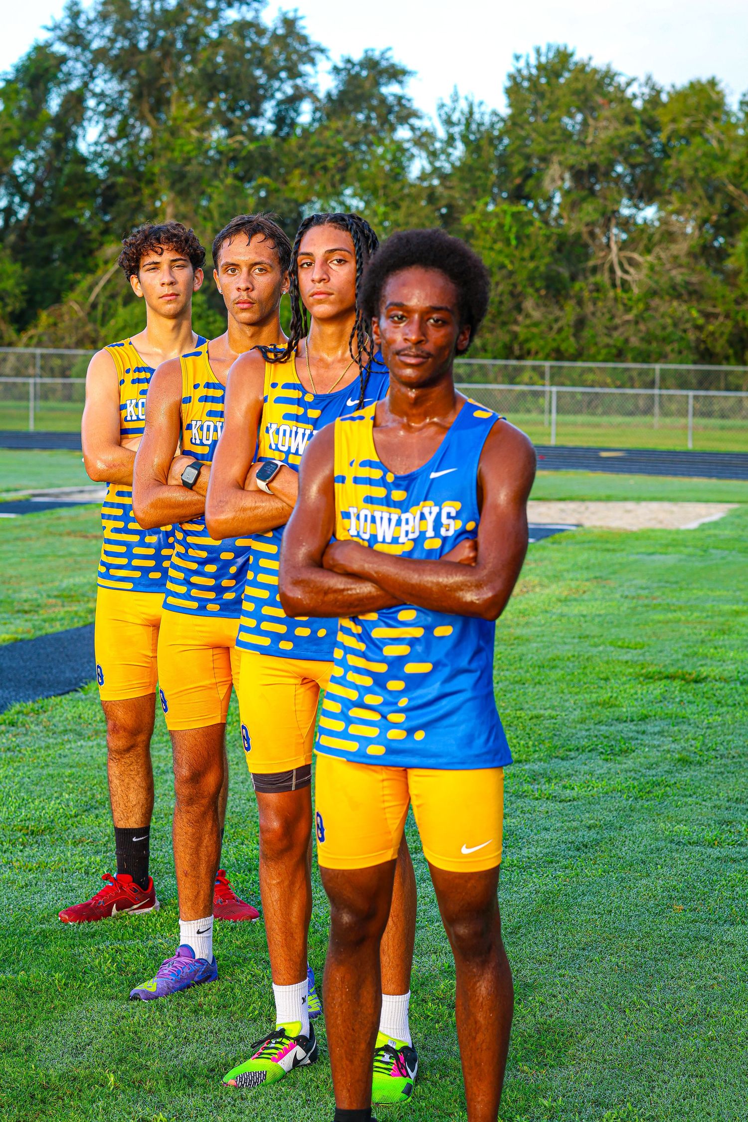 Track and field team members in blue and yellow uniforms pose on grass field during outdoor practice session.