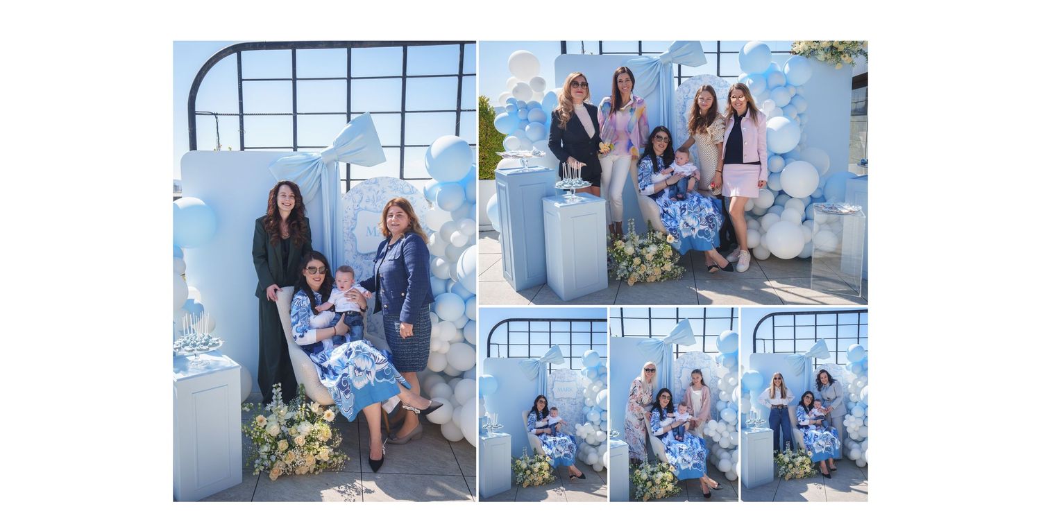A group of people in coordinating blue outfits pose together for outdoor family portraits near a white wall.