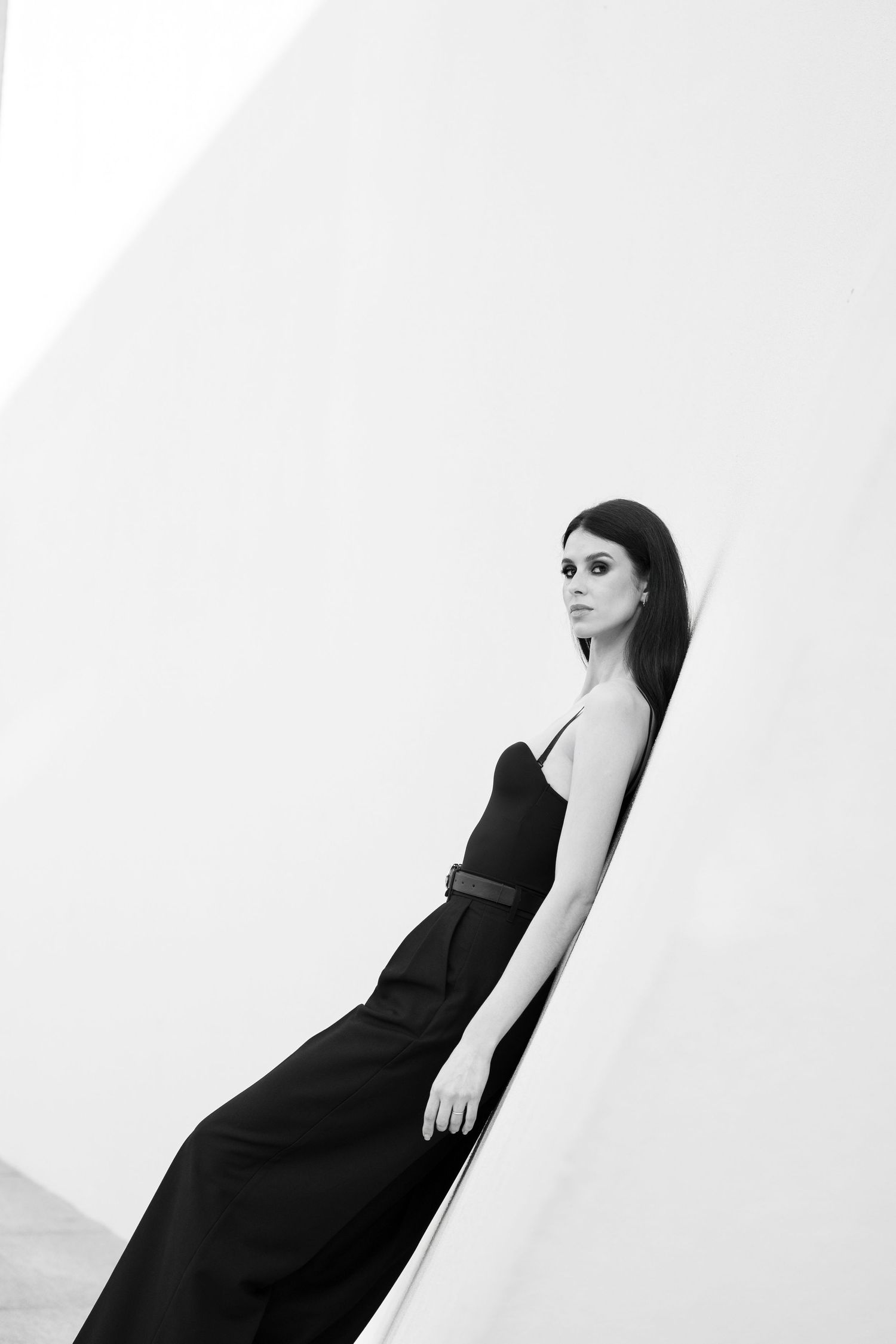 Woman in black dress poses elegantly against white backdrop in artistic monochrome portrait series.
