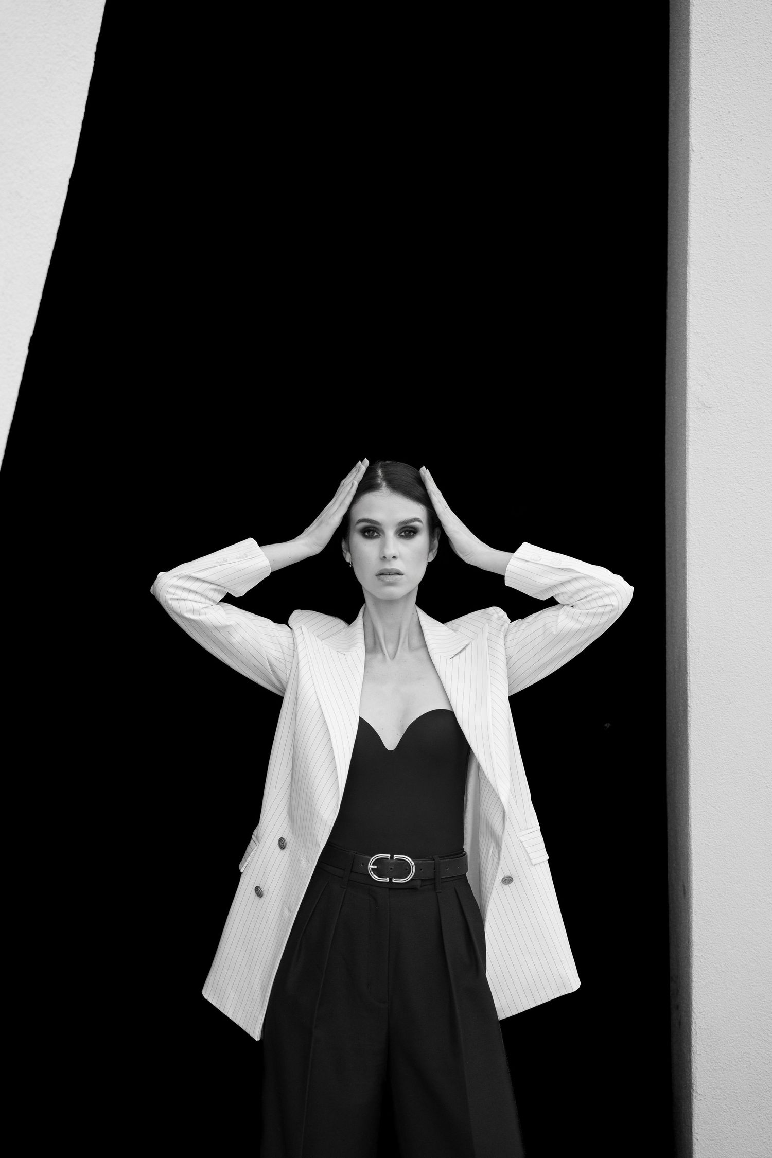 Fashion model wearing black outfit with white blazer in stark monochromatic studio setting.