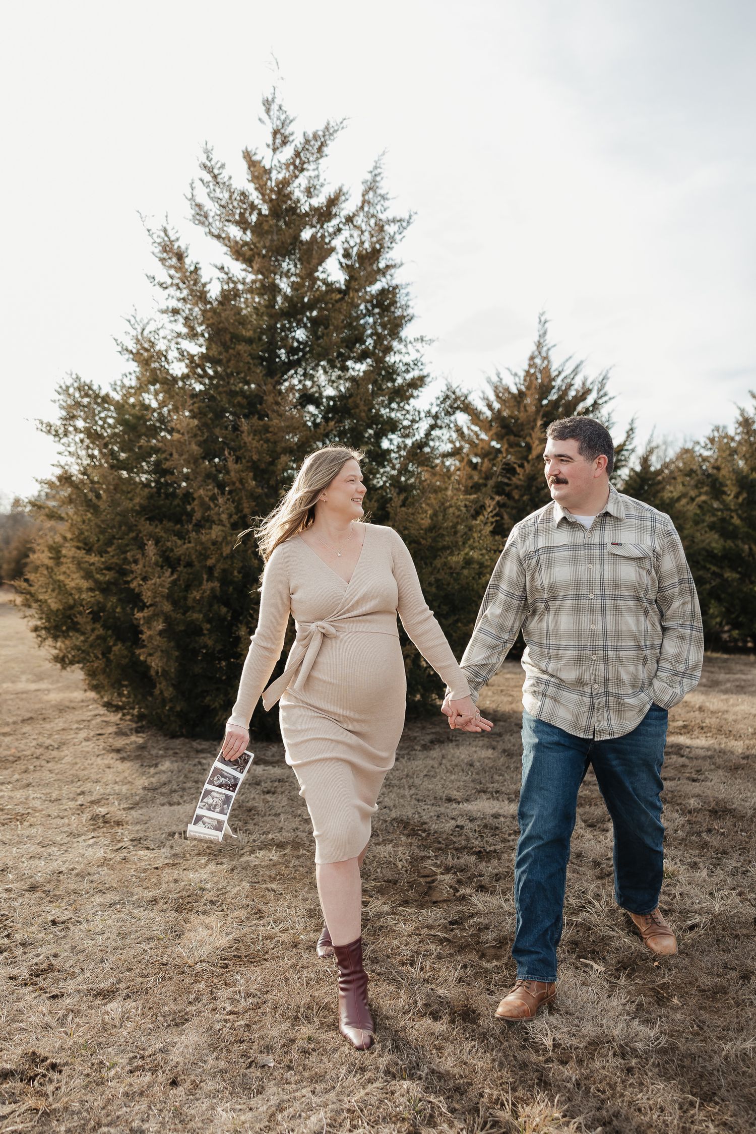 pregnant mother to be holds sonogram photos and husbands hand while walking during photo session as date night ideas in kansas city