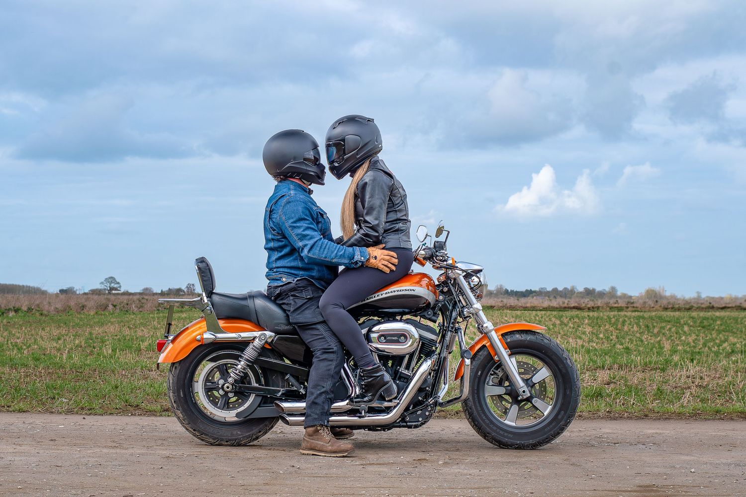 A series of motorcycles and riders lined up on a road against a scenic rural landscape with open fields.