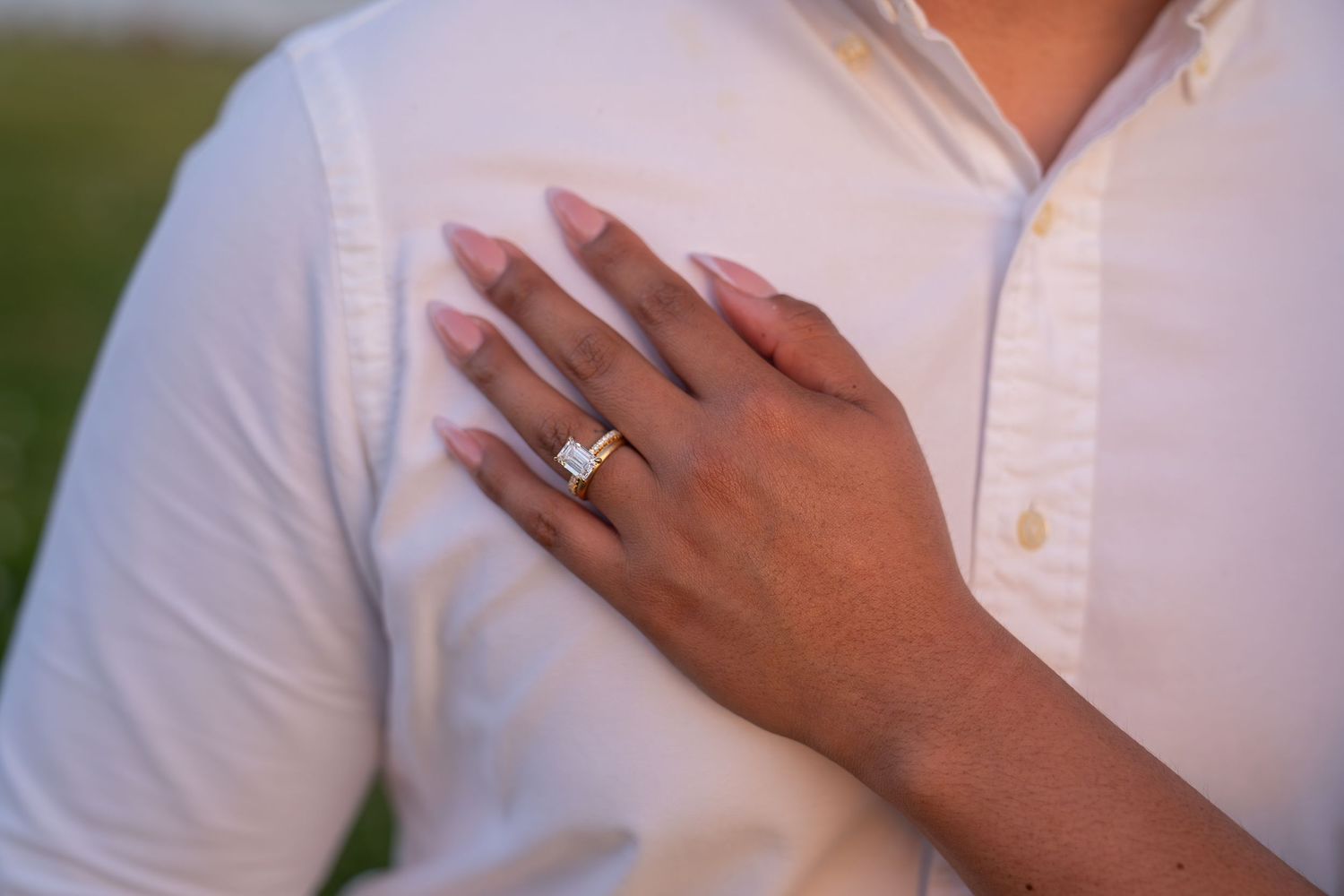 Close-up of a woman's hand with a diamond engagement ring and wedding band resting on a man's white dress shirt.