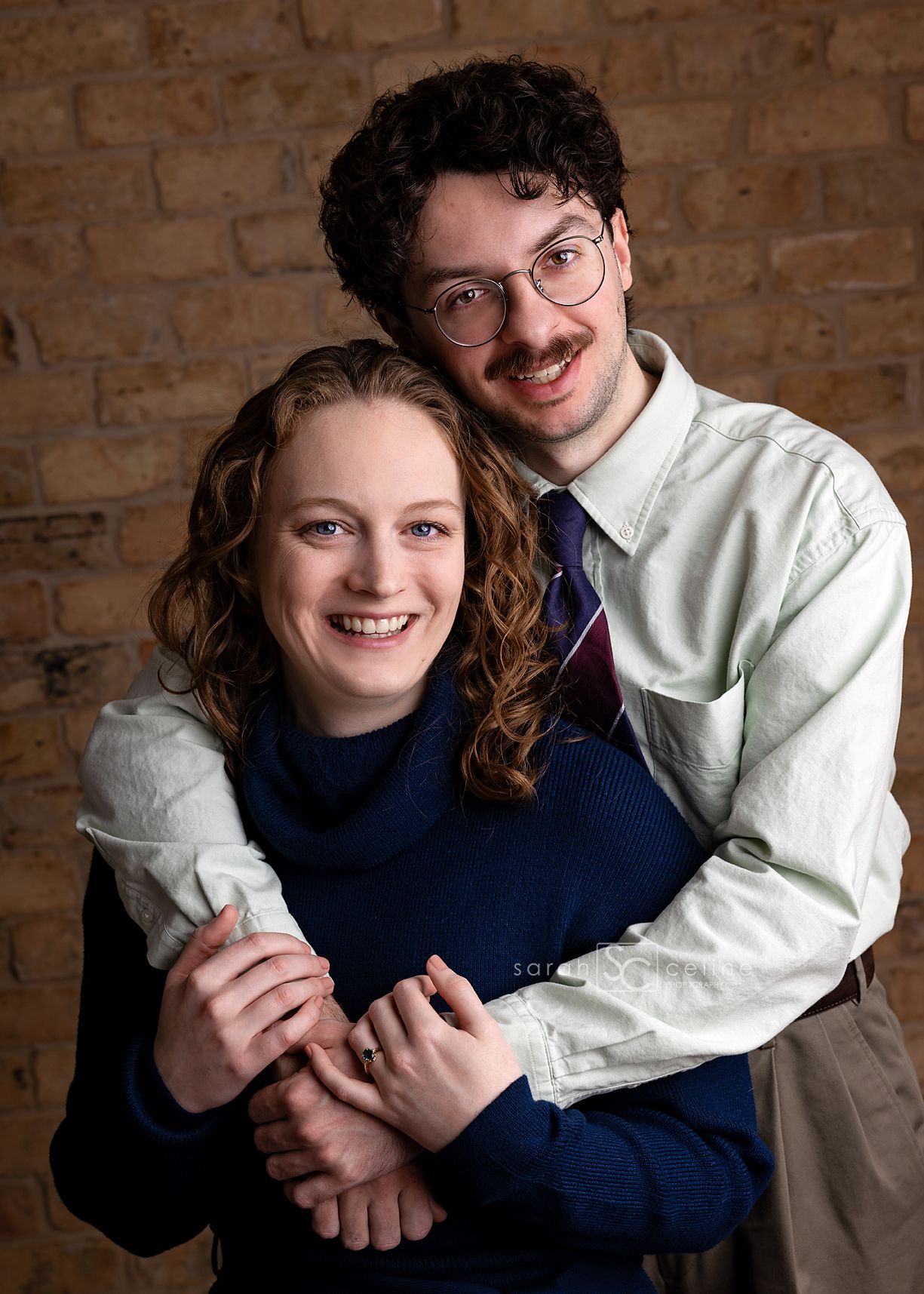 A couple embraces in front of a brick wall, wearing a navy sweater and white shirt, shown in a series of candid moments.